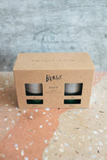 A kraft paper box for Bergs Hoff planter pots with sauces in grey and emerald shown through two window cutouts set on a terrazzo surface against a textured gray wall.
